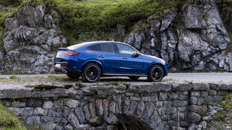 <p>Vista lateral de Mercedes-Benz GLC Coupé color azul siendo conducida cobre puente rocoso.</p>