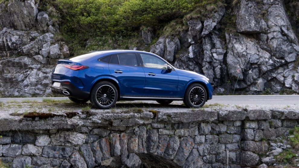 <p>Vista lateral de Mercedes-Benz GLC Coupé color azul siendo conducida cobre puente rocoso.</p>