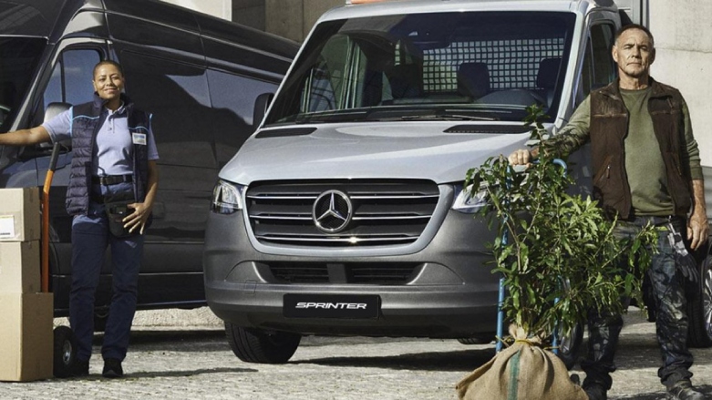Personas con cajas de cartón de pie frente a dos Sprinters chasis.